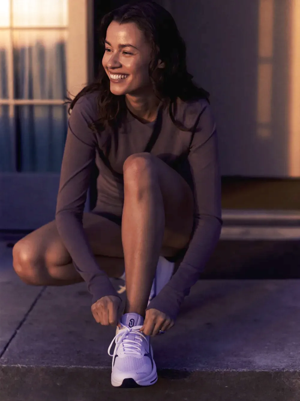 A person lacing up running shoes outdoors at sunrise